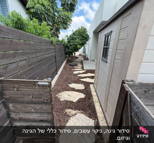 שביל גינה עם אבנים ועצים לצד גדר עץ
